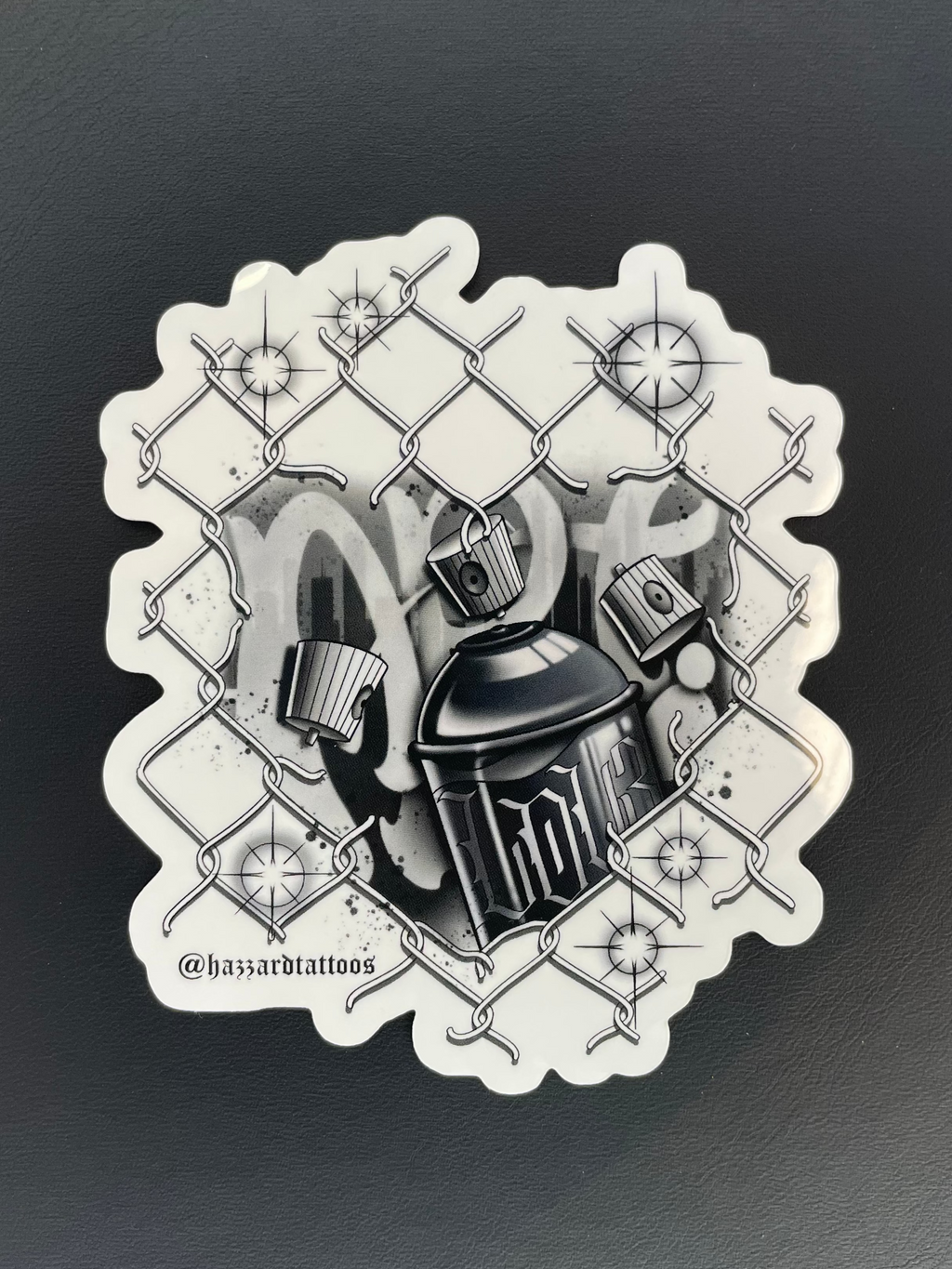 Black and white tattoo design of a spray paint can and chain link fence on a dark background